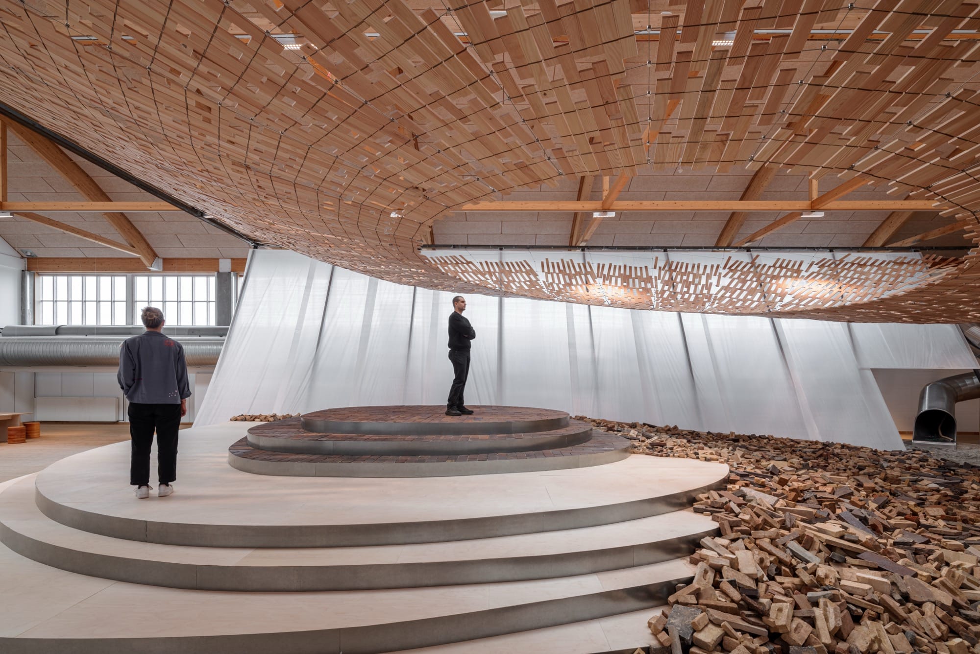 visitors enjoy an installation in which light streams through a wooden canopy by Kengo Kuma