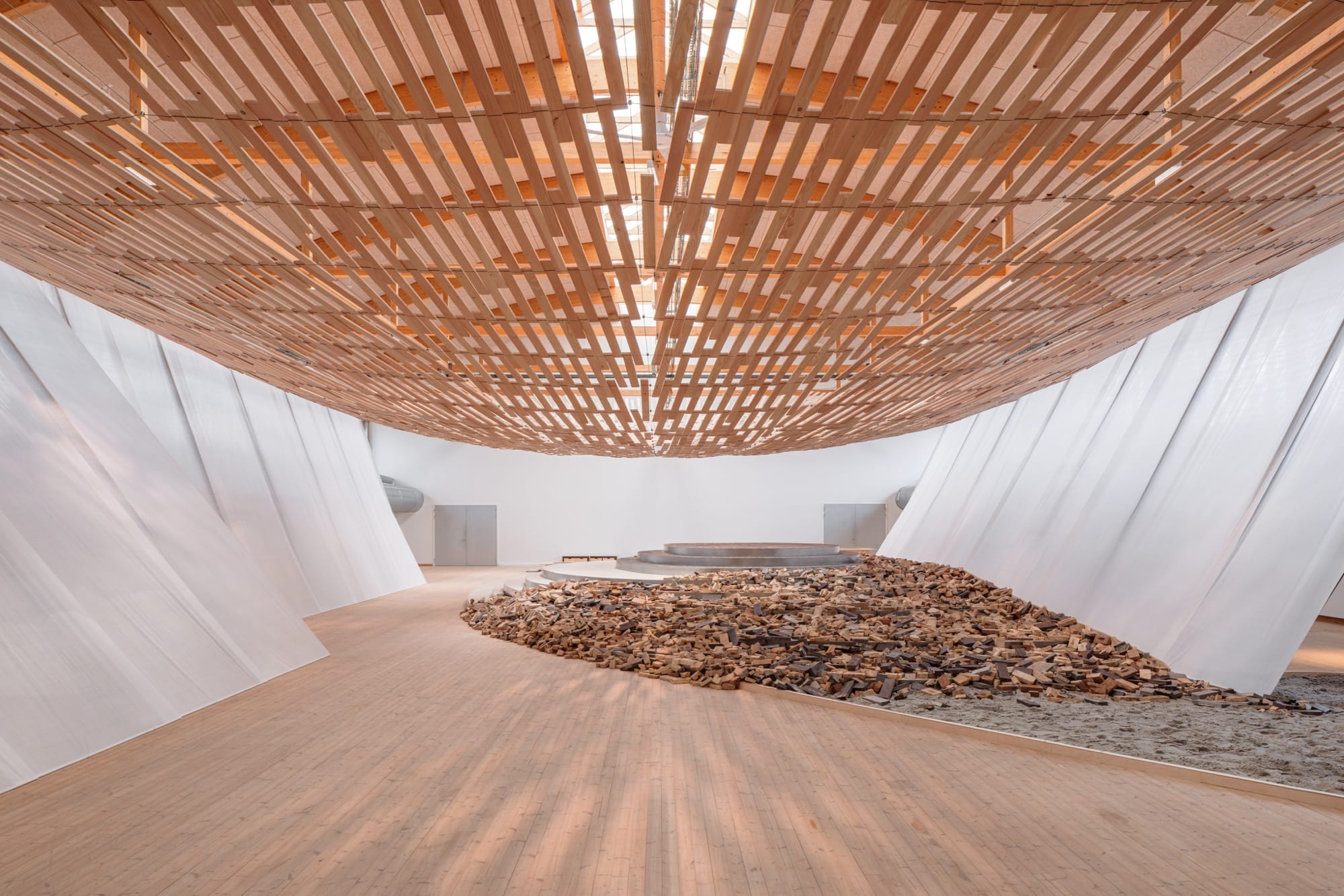 light streams through a wooden canopy in a large scale installation of wood and brick by Kengo Kuma