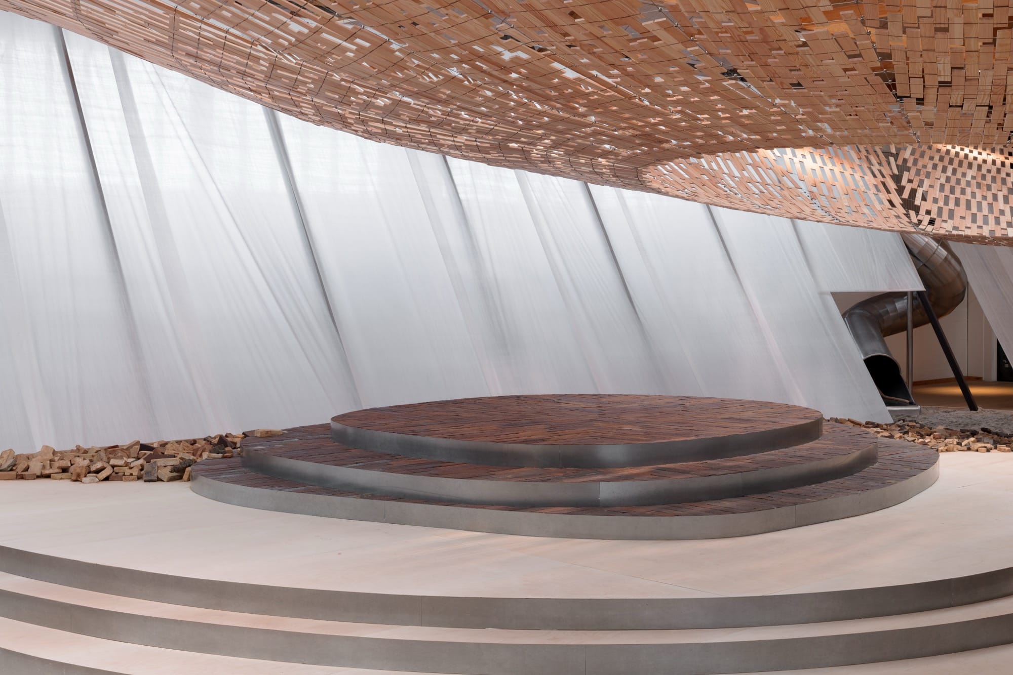 light streams through a wooden canopy in a large scale installation of wood and brick by Kengo Kuma