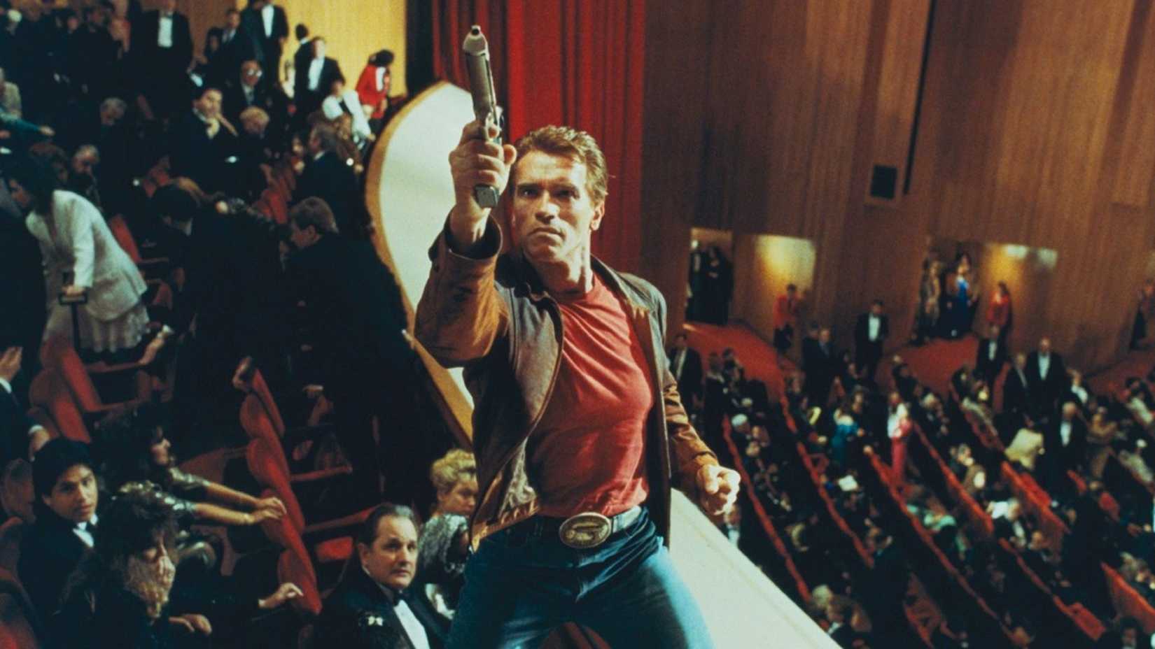 Arnie points a pistol in a crowded movie theater in Last Action Hero