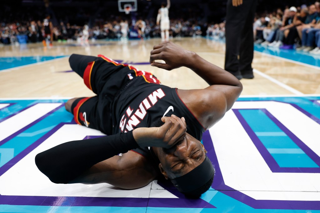 Miami Heat center Bam Adebayo (13) lies on the court, holding his face in pain.