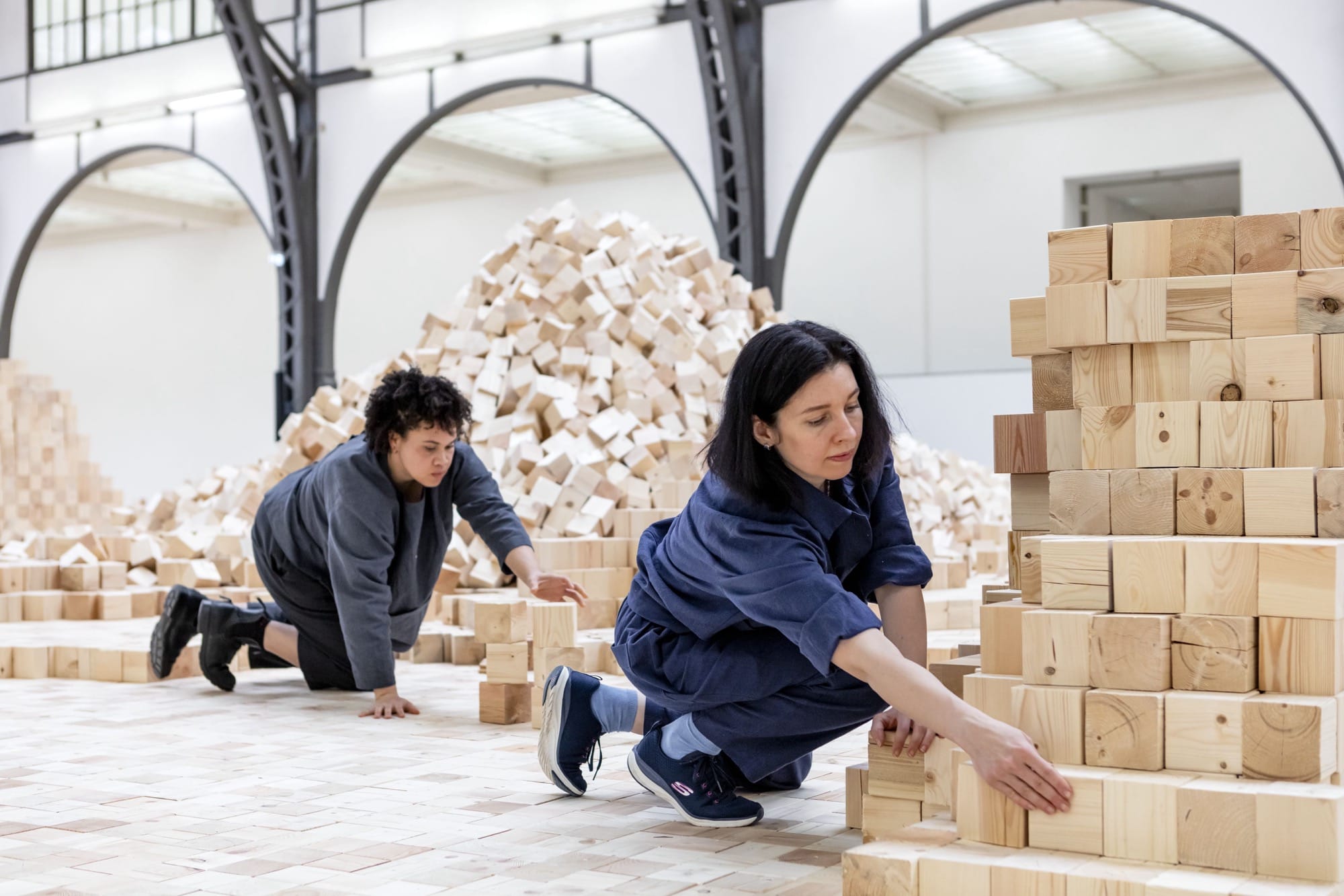 people work on an installation of wooden blocks by Lina Lapelytė in a cavernous building