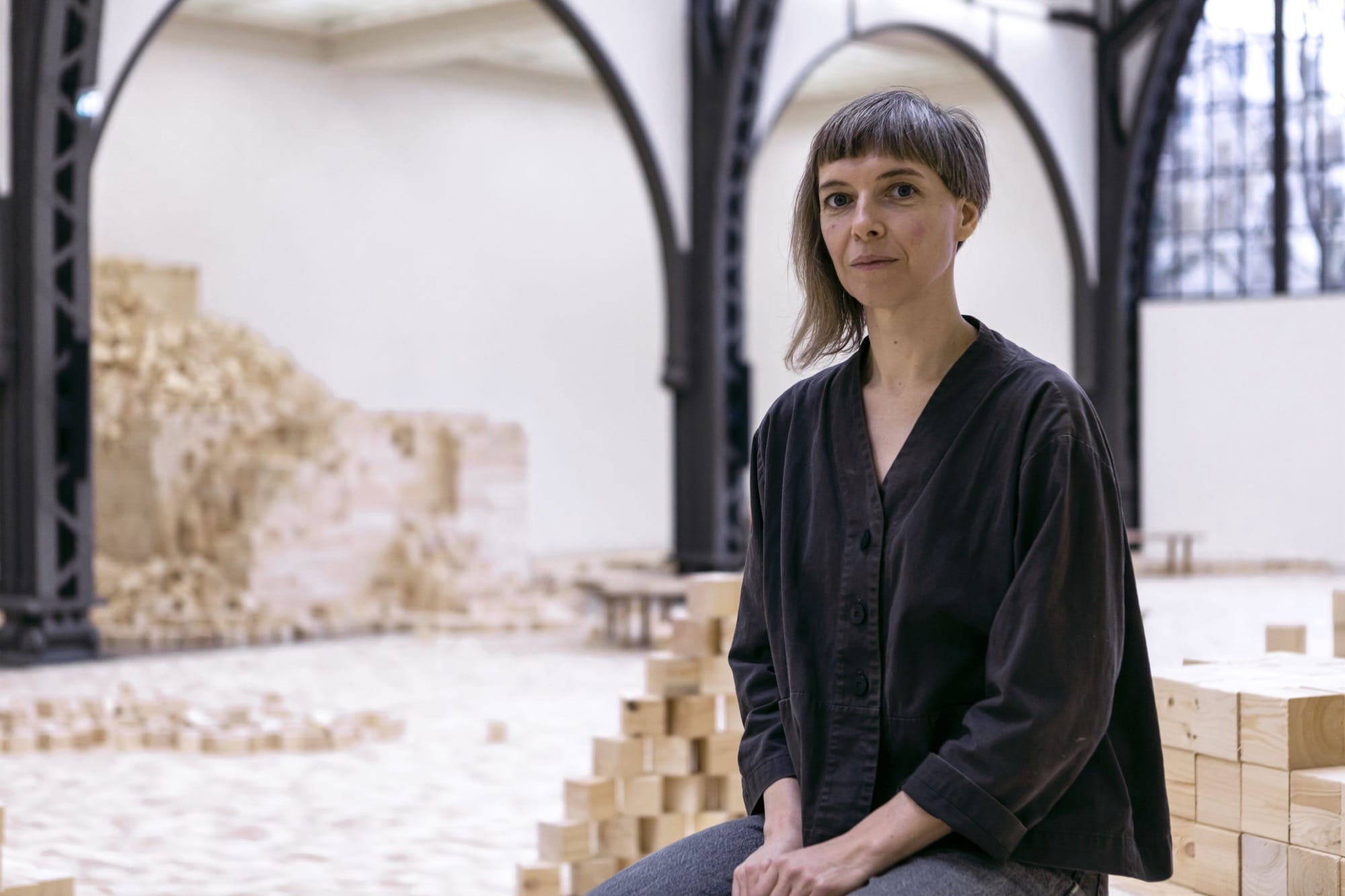 the artist poses with an installation of wooden blocks by Lina Lapelytė in a cavernous building