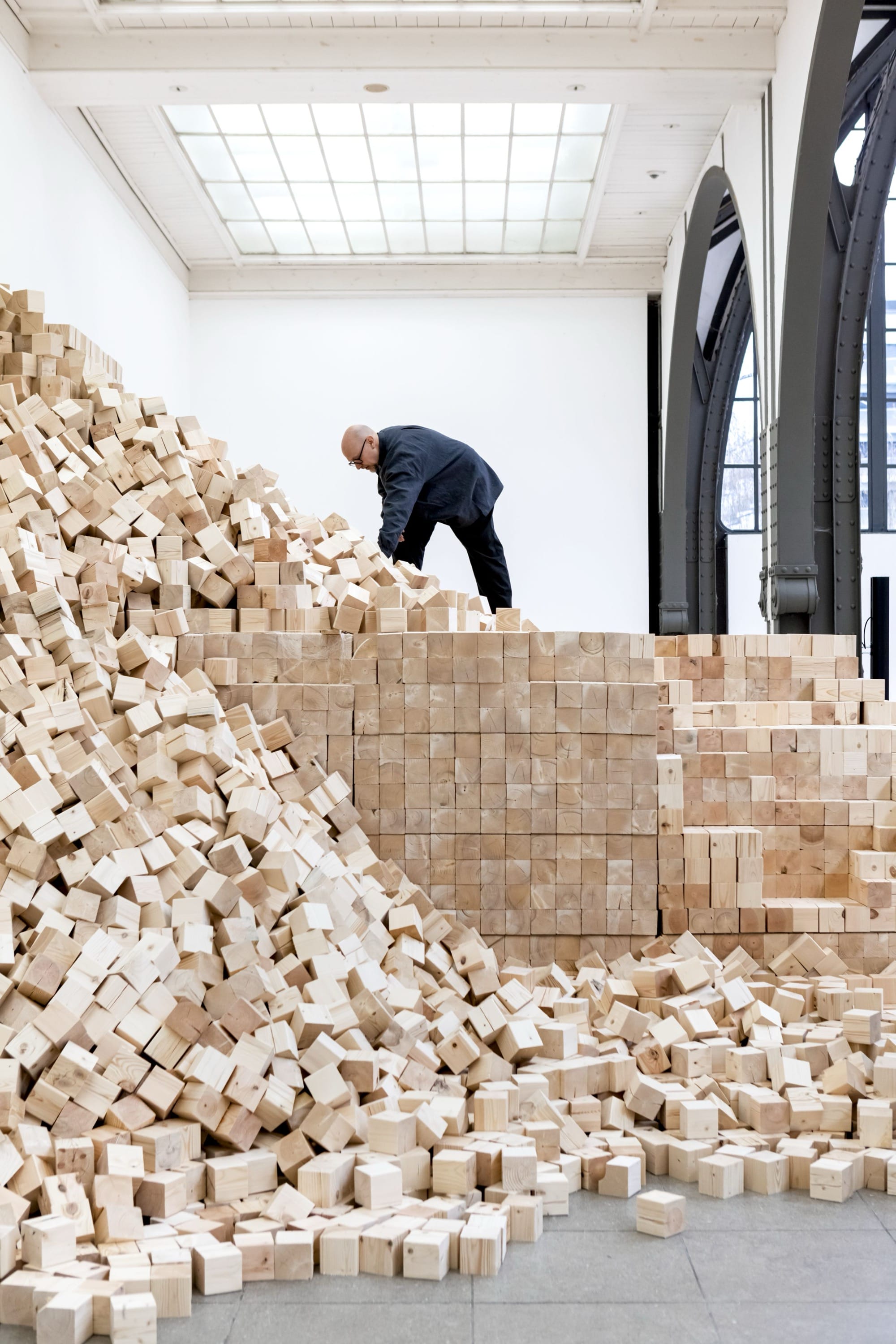 a man works on an installation of wooden blocks by Lina Lapelytė in a cavernous building