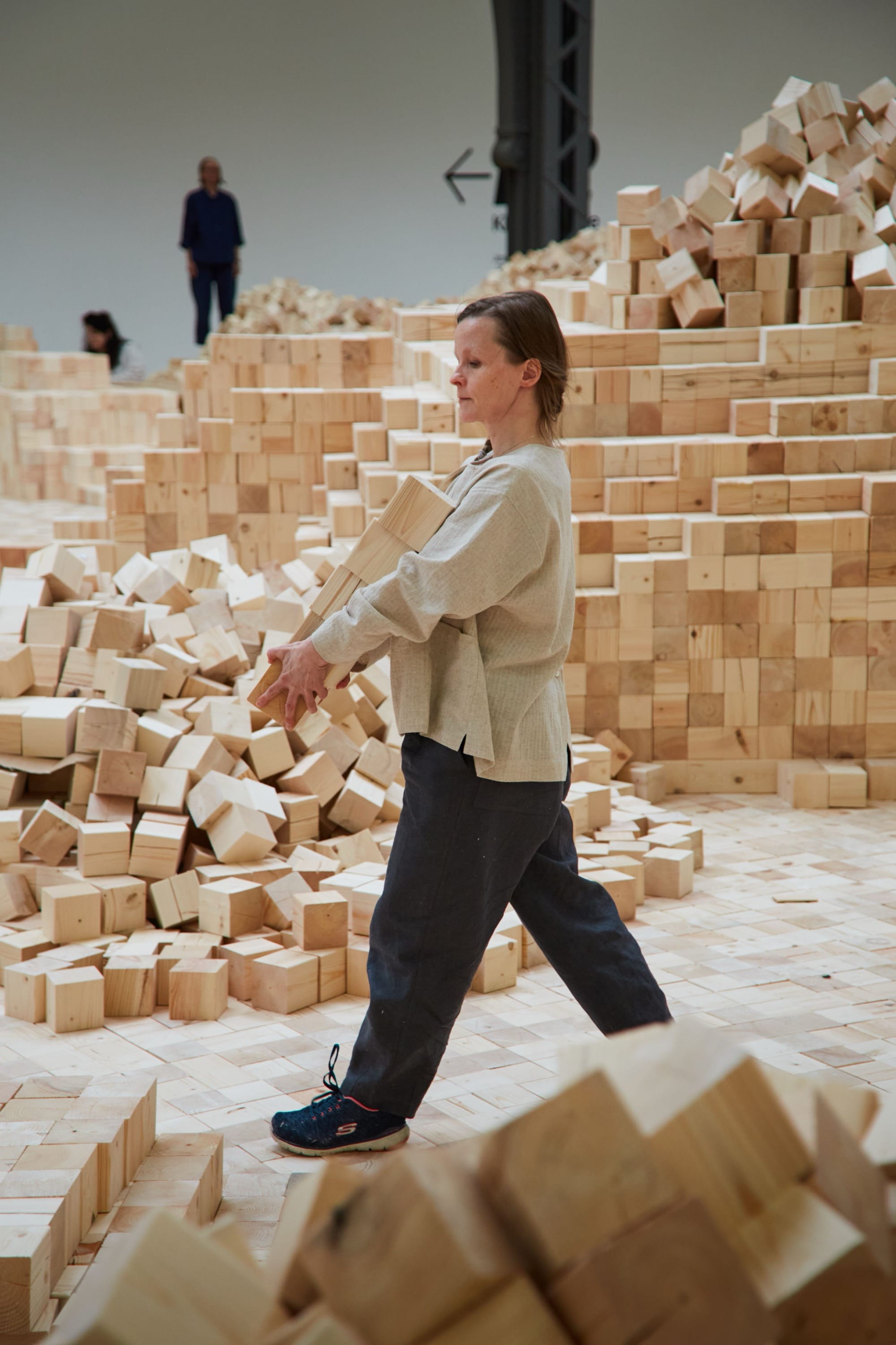 a woman works on an installation of wooden blocks by Lina Lapelytė in a cavernous building