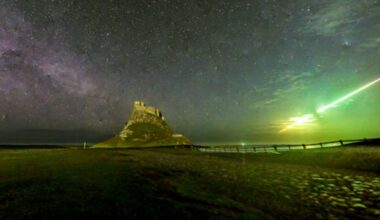 Photograph of Lindisfarne Castle at night with the band of the Milky Way on the left of the image and a streaking line of green light on the right hand side