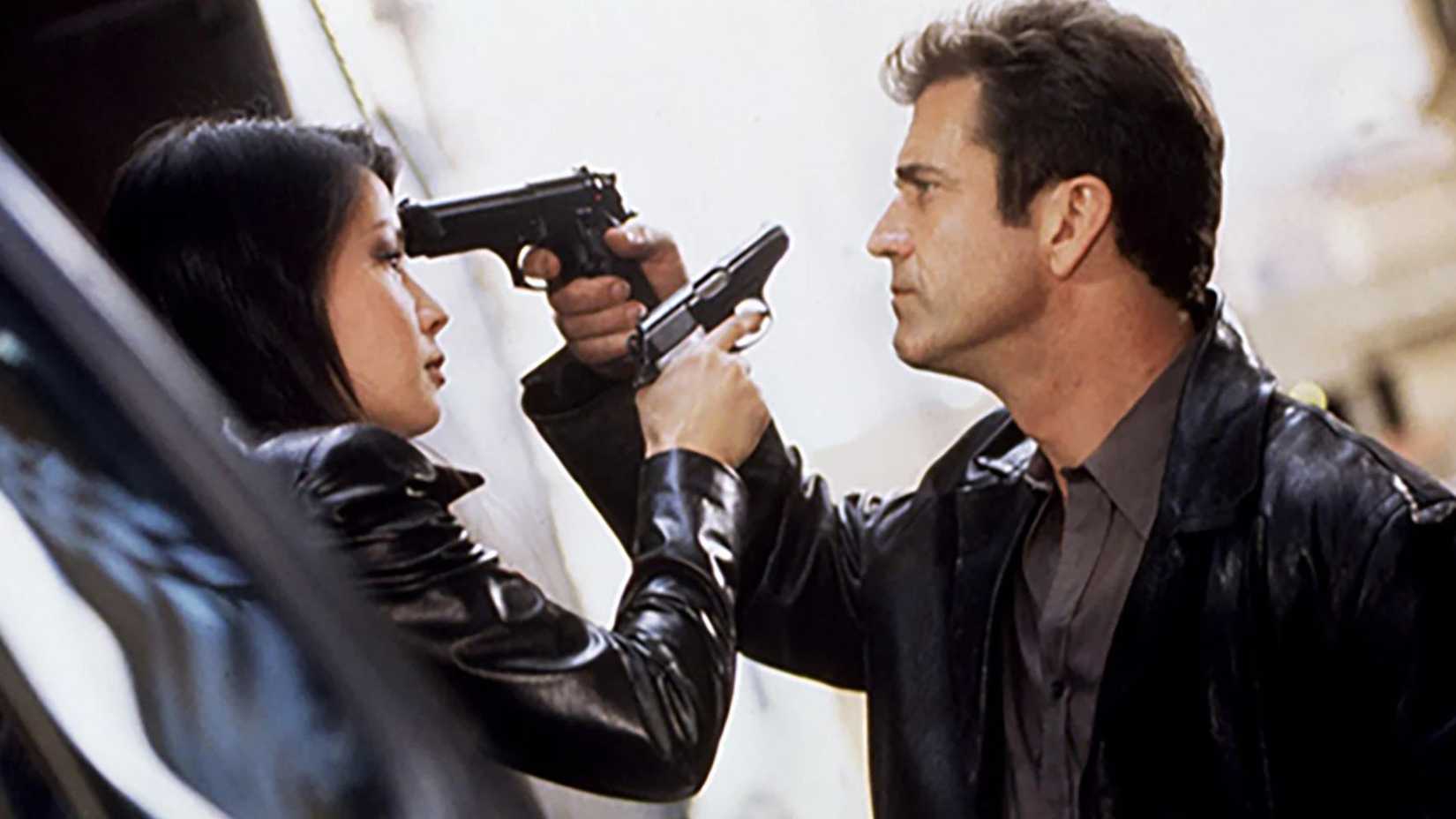Mel Gibson and Lucy Liu holding guns to each others heads in Payback