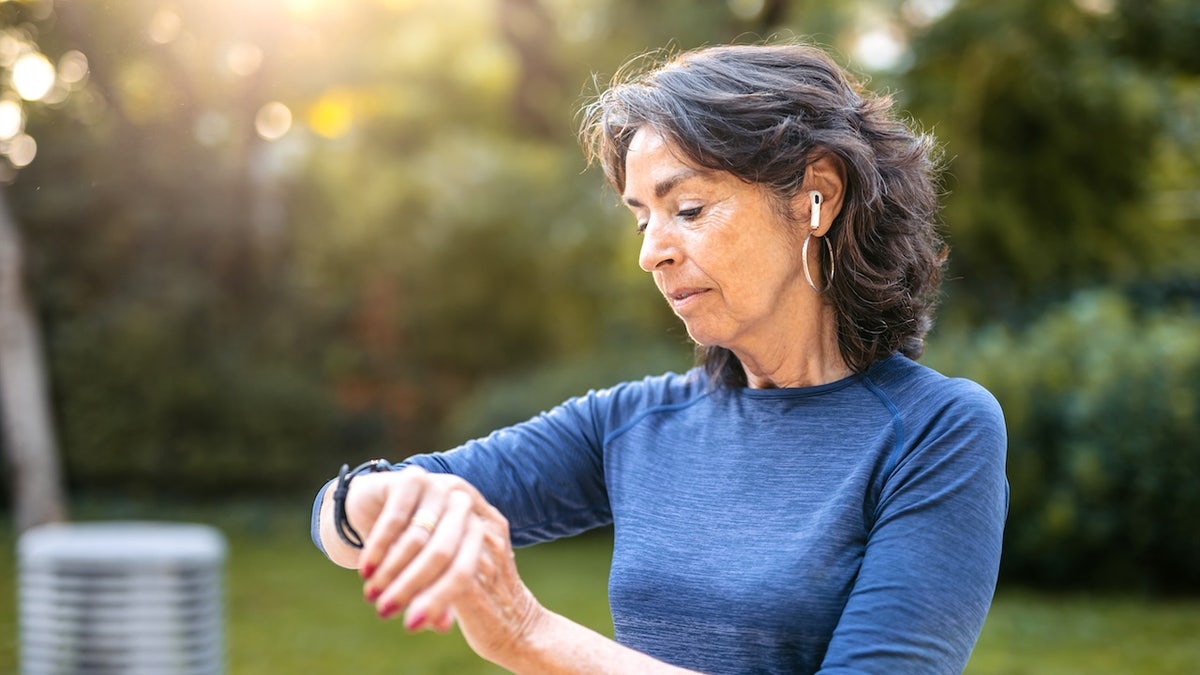 Senior woman checking fitness activity on a smartwatch after jogging in a public park
