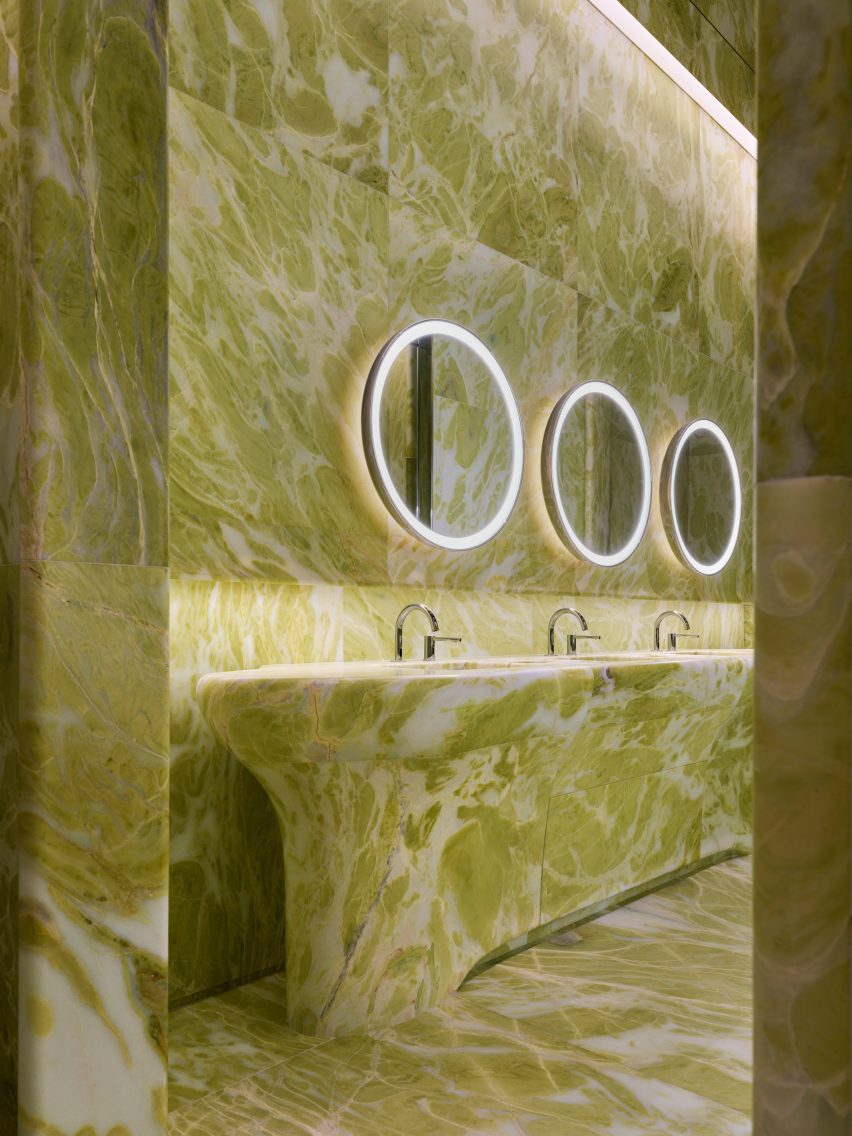 Green marble lines a bathroom, covering the walls and floor, and forming a sculptural basin