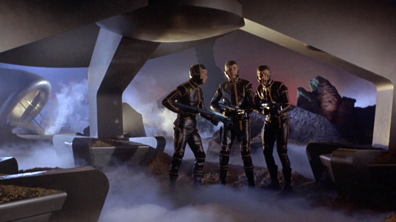 Argos crew members standing under their ship before searching the planet for Galliott in Planet of the Vampires