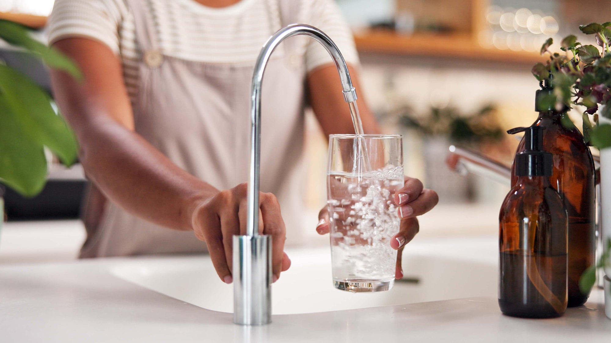 Person pouring water from a faucet into a glass