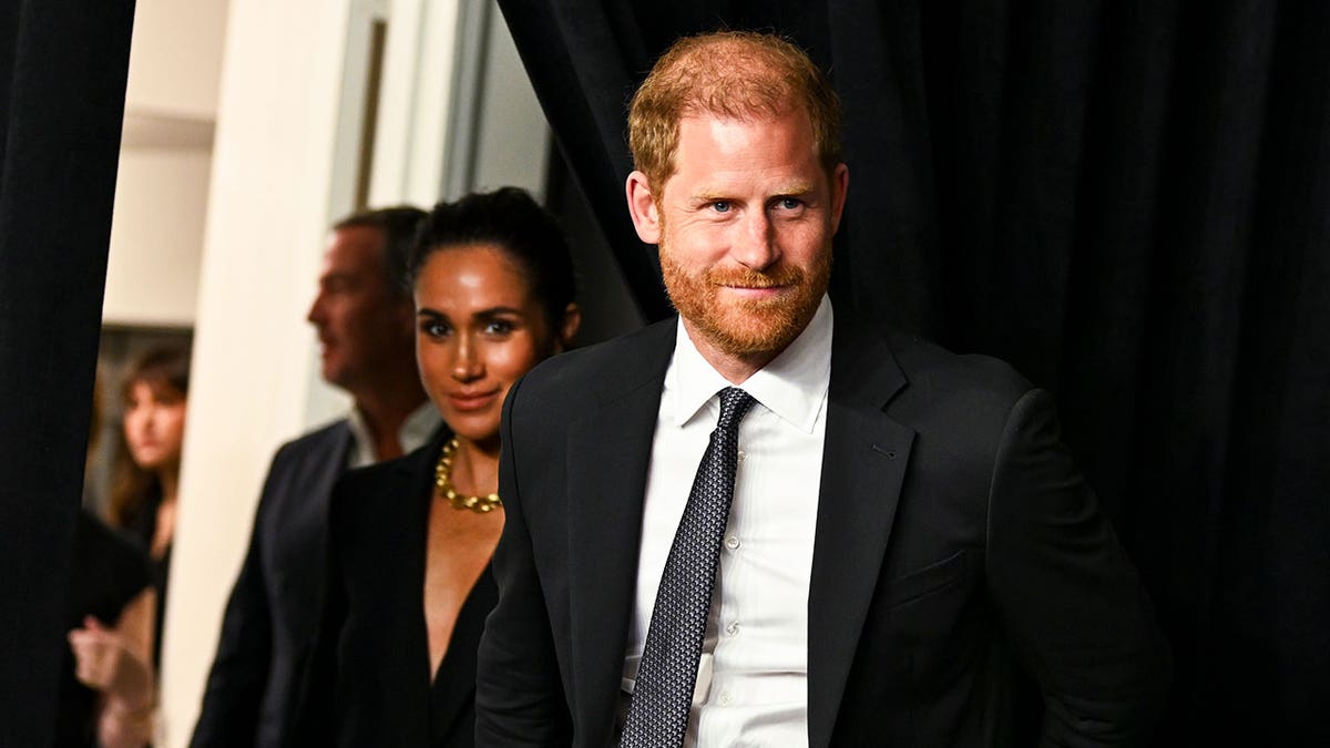 Prince Harry walking ahead of Meghan Markle wearing matching black attire at an event