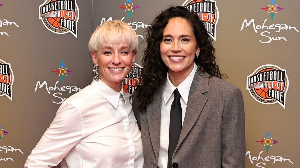 Two people smiling at the Basketball Hall of Fame event, with logos and a Mohegan Sun backdrop.