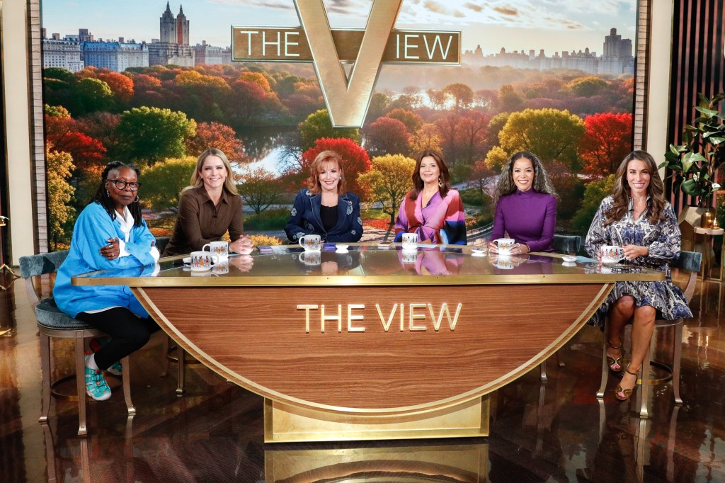 The hosts of The View, Whoopi Goldberg, Sara Haines, Joy Behar, Ana Navarro, Sunny Hostin, and Alyssa Farah Griffin, sitting at their desk in front of a backdrop of Central Park in autumn.