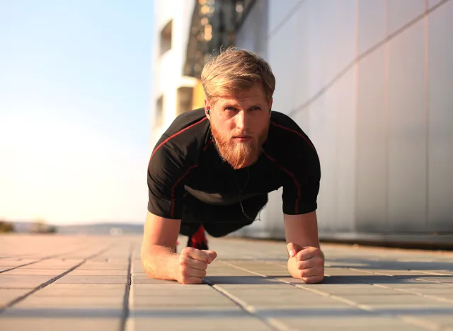 Handsome young man in sports clothing keeping plank position while exercising outdoors
