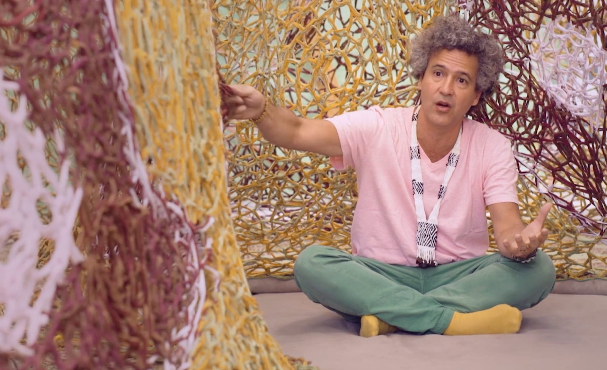 ernesto neto sits on the floor while touching his sculpture
