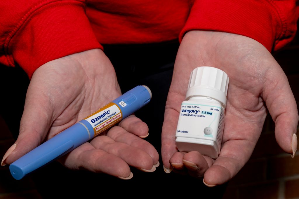 A person holds an Ozempic semaglutide injection pen and a bottle of Wegovy semaglutide tablets.