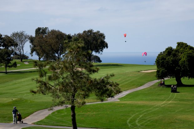 Paragliders sore overhead as a golfer walks down the fairway at Torrey Pines Golf Course on Wednesday, April 1, 2026, in San Diego. (Meg McLaughlin / The San Diego Union-Tribune)