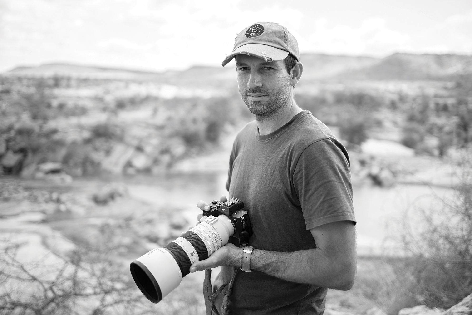Black and white portrait of Will Burrard-Lucas holding a Sony camera and lens