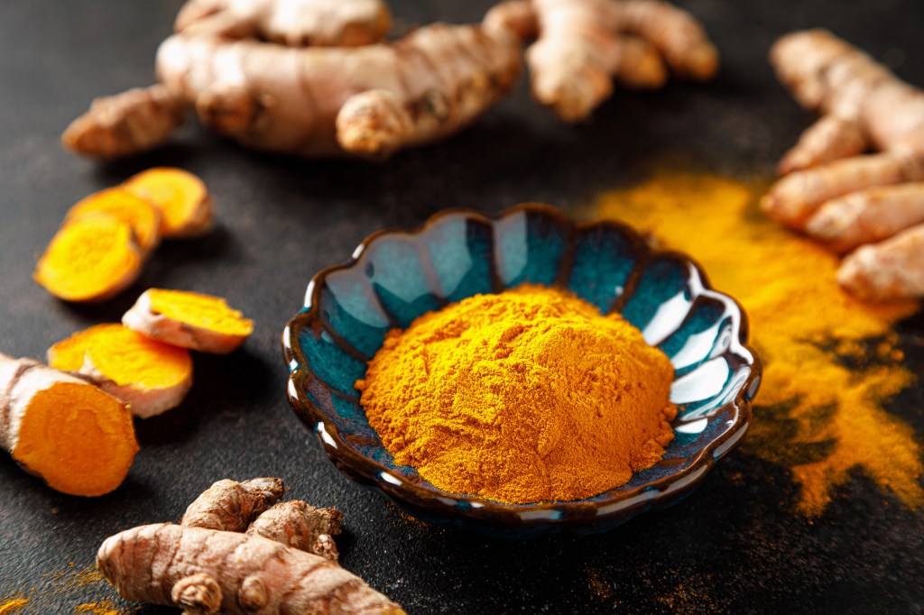 Fresh turmeric root and yellow turmeric powder in a blue bowl.