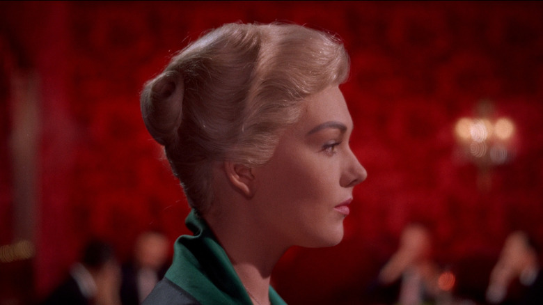 A profile shot of Kim Novak as Judy Barton / Madeleine Elster in Vertigo, standing against a striking red background.