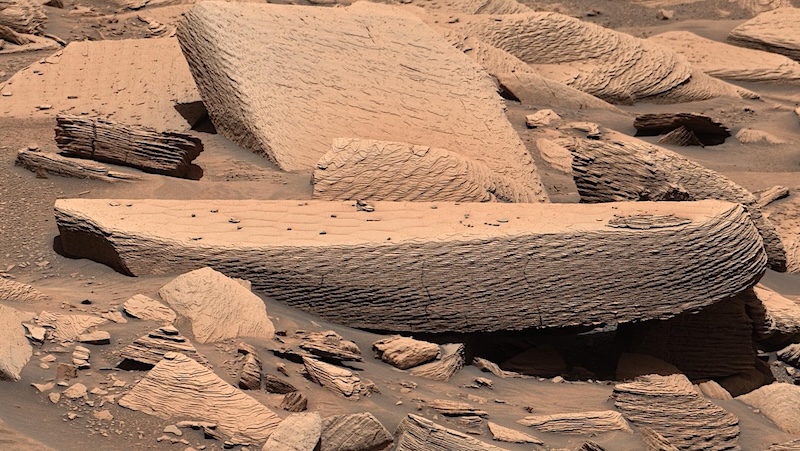 Sandstorm on Mars: Large slabs of brownish, dust-covered rocks, with fine ripple textures on them.