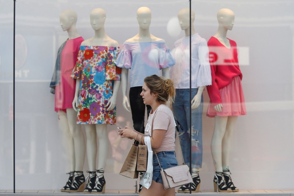 A woman walks past a retail store window display featuring five mannequins.