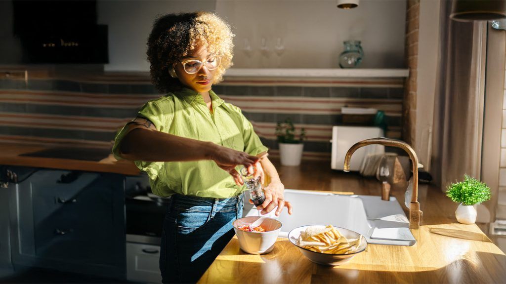 A person prepares a bowl of food, grinding pepper over it next to a bowl of tortilla chips