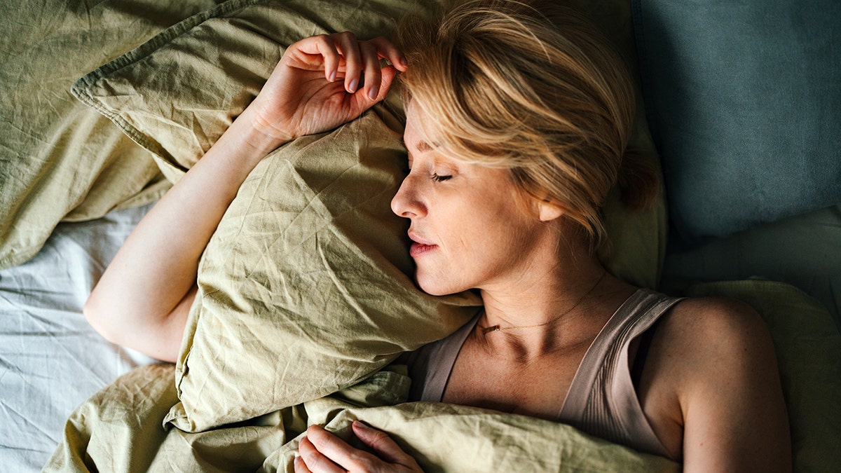 Blonde woman sleeping peacefully on her side in bed resting on a green pillow