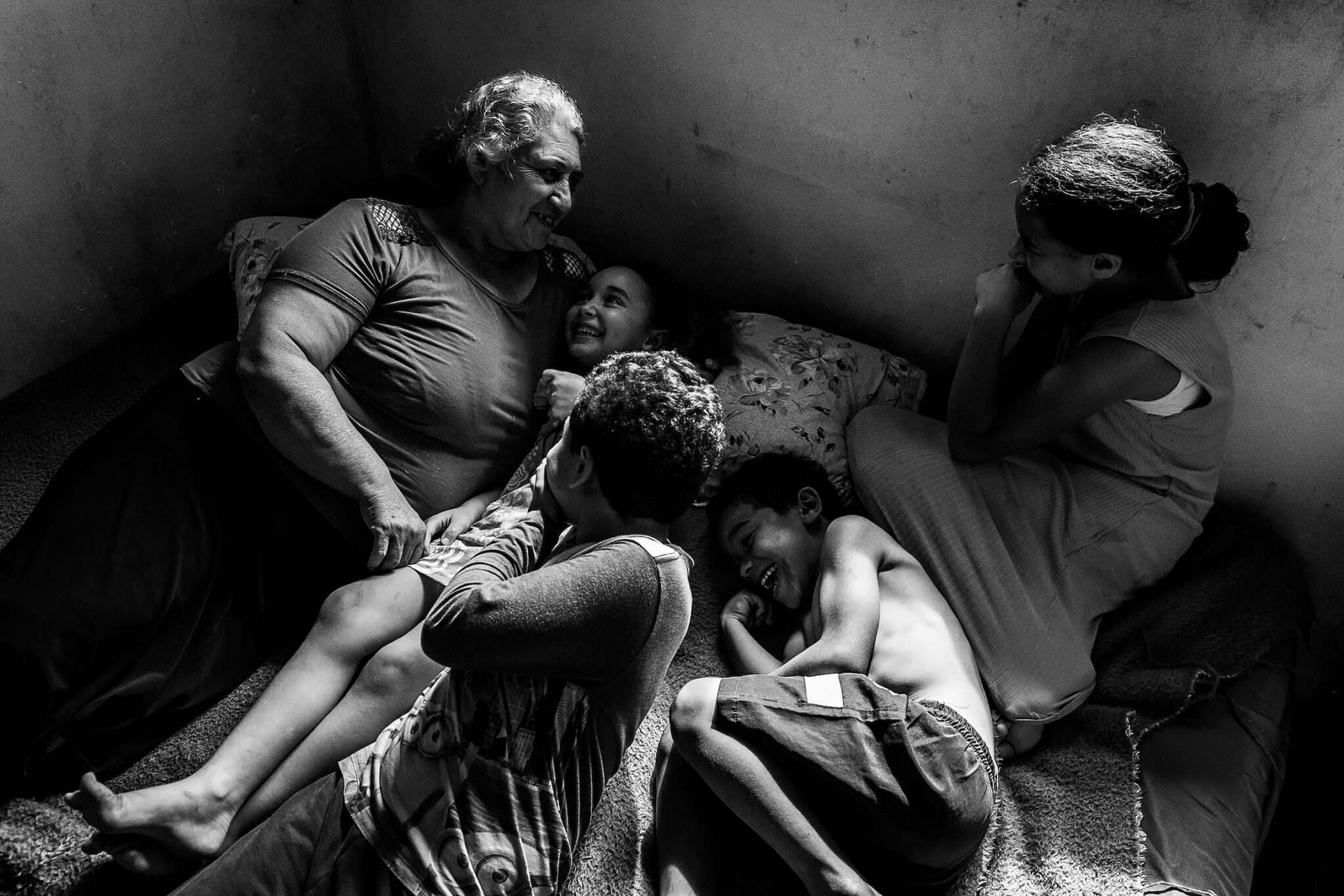 Priscila Ribeiro, “A Territory of Hope.” In the city of Colombo, Brazil, the Parque dos Lagos occupation is home to 200 families living without official access to water, sewage disposal, or electricity. Sandra Mara Siqueira rests with her grandchildren, Micael, Davi, Ana Flávia, and Vitória. Living in the Parque dos Lagos occupation since 2013, the family seeks land regularization to guarantee access to basic infrastructure. Colombo, Paraná, Brazil, November 15, 2025.