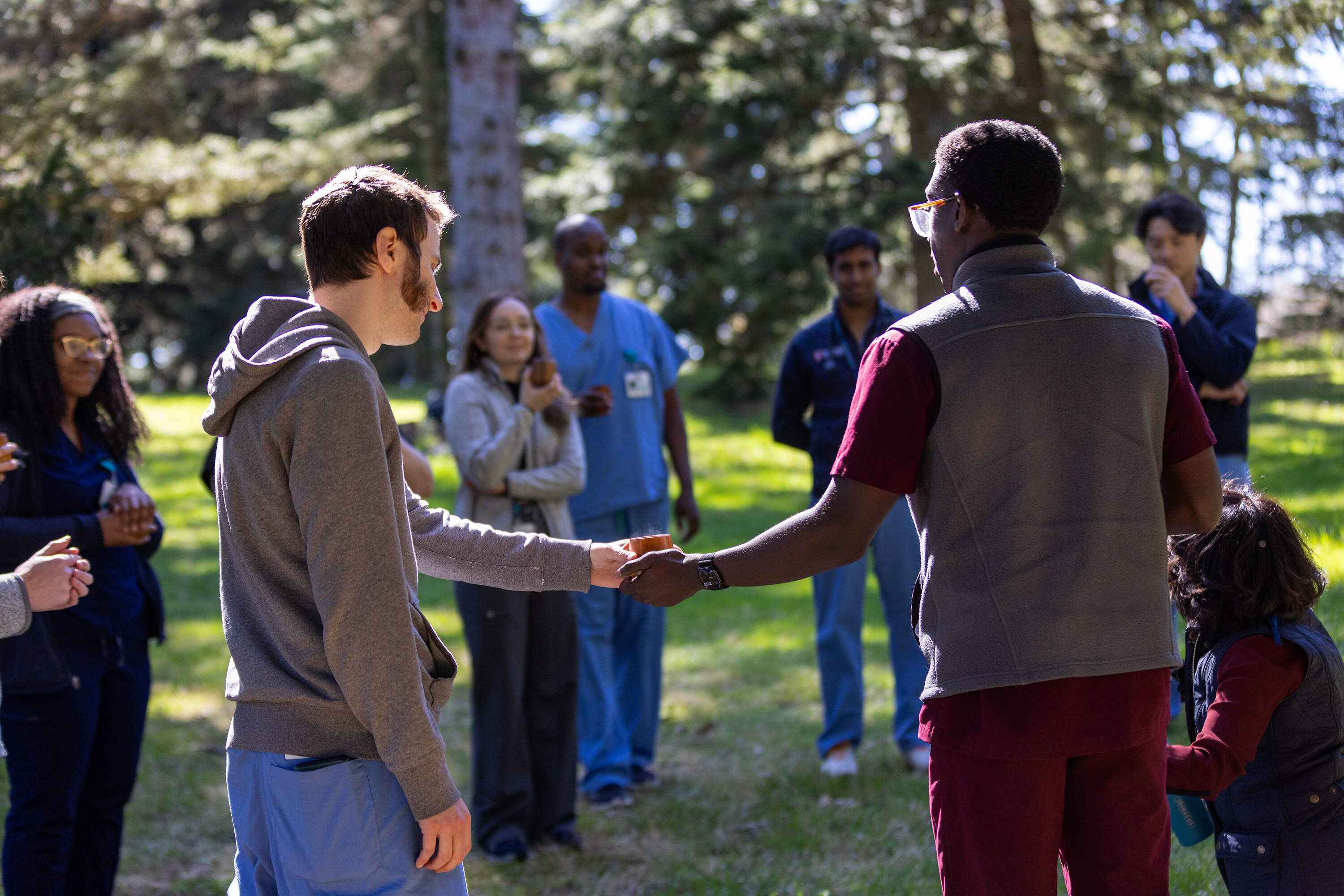 Residents from Brigham and Women's Faulkner Hospital and Harvard Medical School students pass cups of birch tea around a circle to conclude a forest therapy session at the Arnold Arboretum. (Jesse Costa/WBUR)