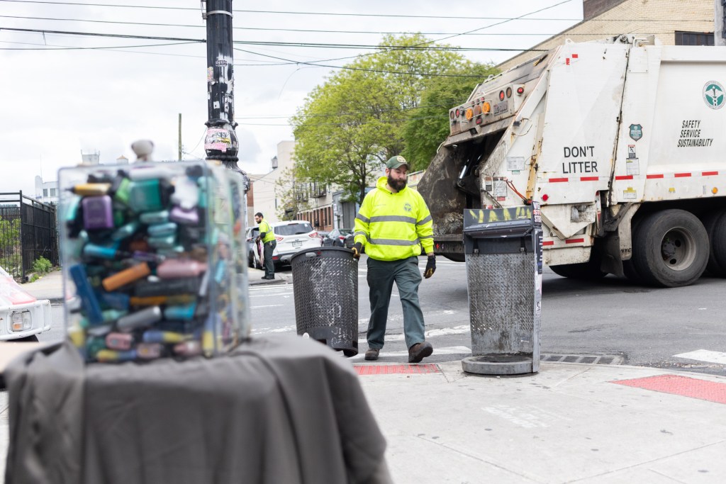 Department of Sanitation workers collect garbage next to a vape recycling box in Bushwick,