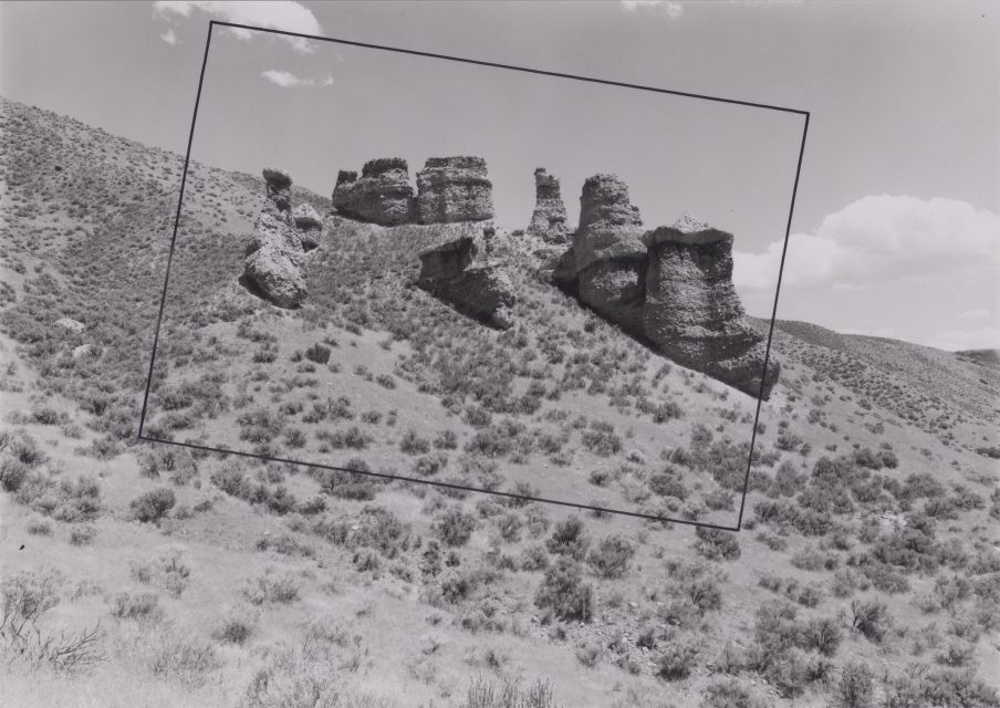 Black-and-white photo of rocky outcrops on a shrub-covered hillside, with a rectangular outline superimposed over part of the rock formations.