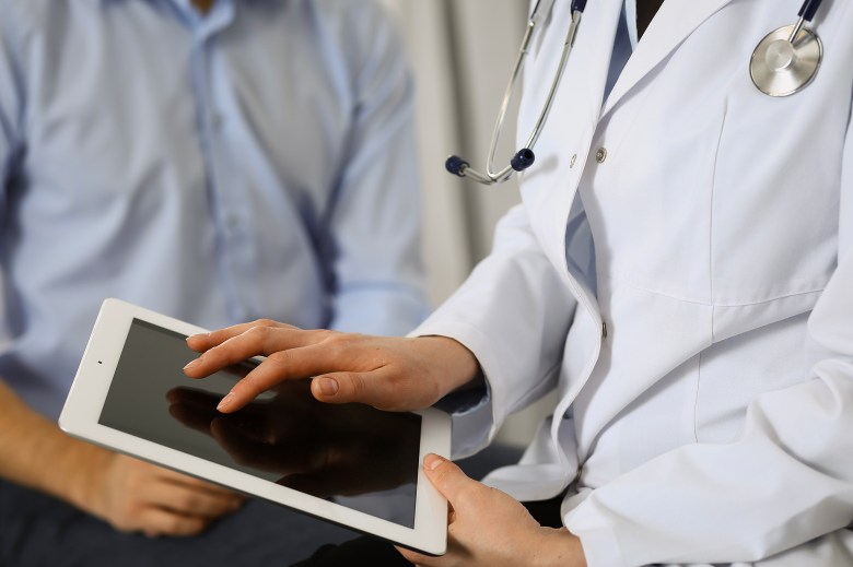 Female doctor using touchpad or tablet computer while consulting man patient in hospital.