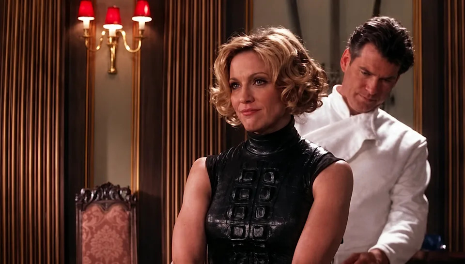 Two characters from a movie scene: one sits in a futuristic black outfit, while another stands behind in a chef's uniform