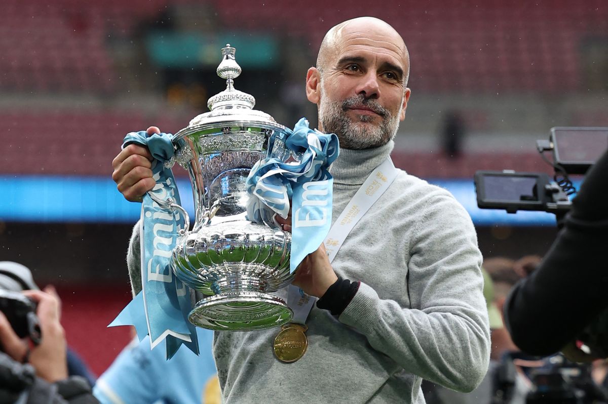 Manchester City's Spanish manager Pep Guardiola poses with the trophy on the pitch after the English FA Cup final football match between Chelsea and Manchester City at Wembley Stadium in London, on May 16, 2026. Manchester City won the game 1-0