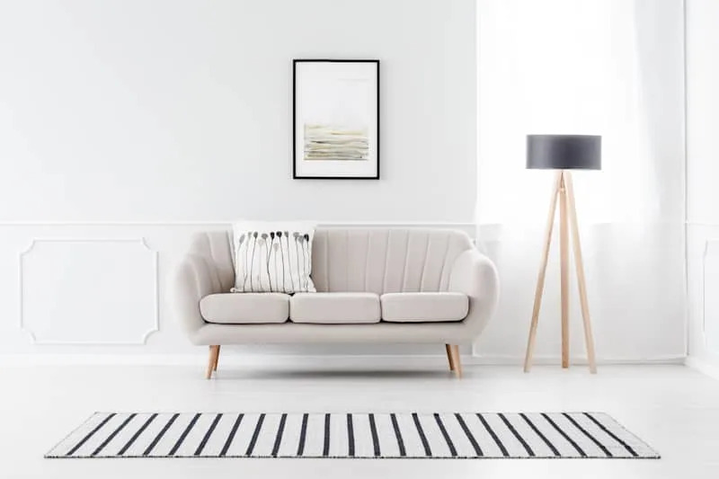 Beige couch standing against white wall with molding and watercolor poster in cozy living room interior