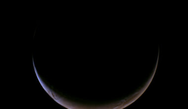 A slender, glowing crescent of Mars curves across the bottom of a completely black void, revealing its dusty reddish-orange surface and a thin, hazy blue atmospheric glow along the illuminated edge.
