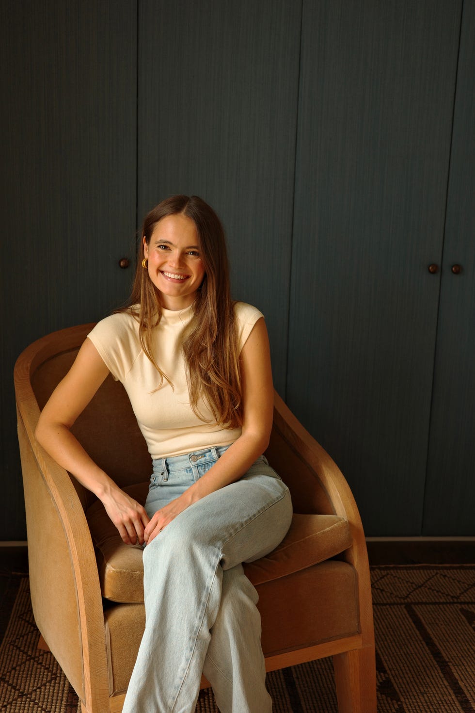 Person seated in a chair against a wooden backdrop.