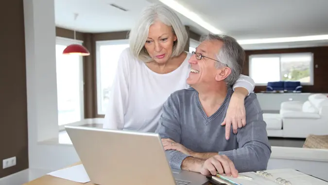 Senior couple using laptop and celebrating a win with their finances, retirement planning, Social Security and more.