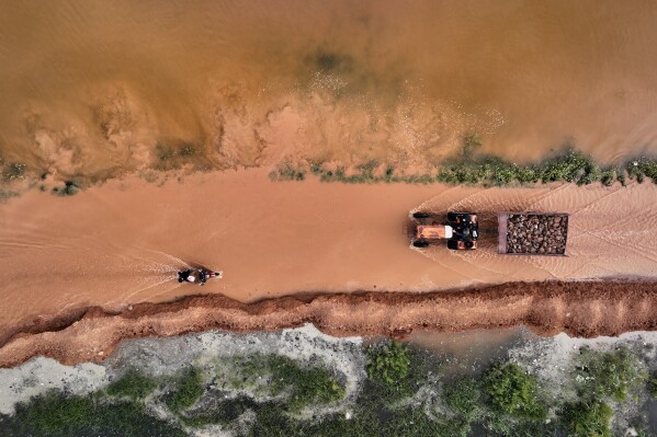 A tractor and a motorcycle make their way through muddy floodwaters covering a road after heavy rains raised water levels at the Al-Siha Dam, affecting nearby villages and farmland near Abu al-Duhur, northwestern Syria, Saturday, April 25, 2026. (AP Photo/Ghaith Alsayed, File)