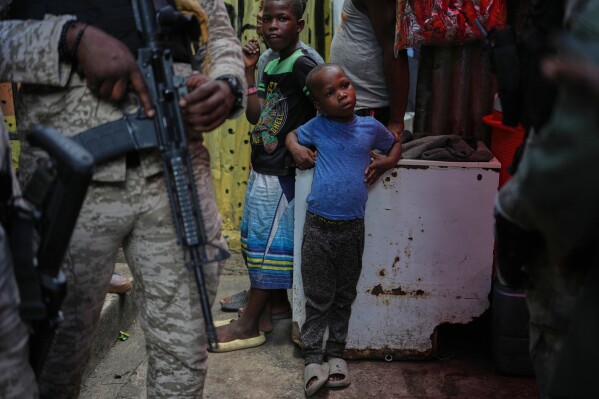 Children stand next to police officers during a visit from World Food Programme advisor Princess Sarah Zeid of Jordan at a shelter for families displaced by gang violence in Port-au-Prince, Haiti, Monday, April 27, 2026. (AP Photo/Odelyn Joseph, File)