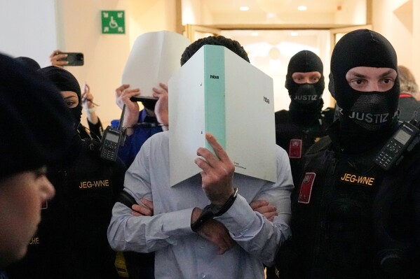 The defendants hide their faces behind file folders on their way to the courtroom in the District Court in Wiener Neustadt, Austria, where two terror suspects will stand trial Tuesday, one for plotting to carry out an attack on one of superstar singer Taylor Swift's concerts in Vienna in August 2024 and pledging allegiance to the Islamic State group, Tuesday, April 28, 2026. (AP Photo/Matthias Schrader, File)