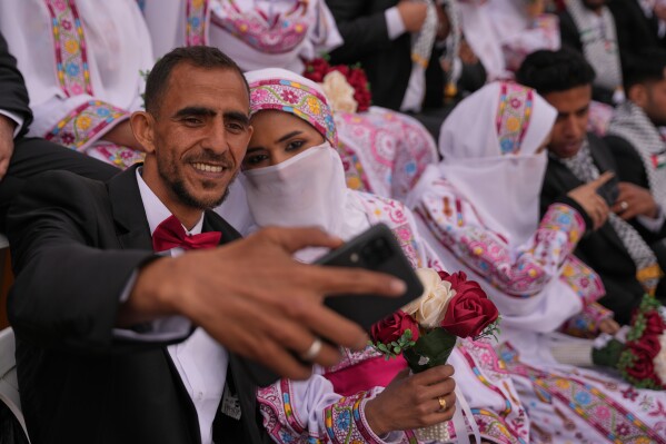 A Palestinian couple poses for a selfie as they get married in a mass wedding ceremony in Deir al-Balah, central Gaza Strip, Friday, April 24, 2026. (AP Photo/Abdel Kareem Hana, File)