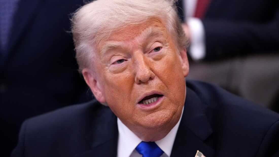 President Trump holds an executive order signing in the Oval Office of the White House. He is seen from the shoulders up, wearing a dark suit and blue tie.