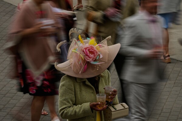 A woman holds drinks as people pass before the 152nd running of the Kentucky Derby horse race at Churchill Downs, Saturday, May 2, 2026, in Louisville, Ky. (AP Photo/Charlie Riedel)