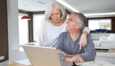 Senior couple using laptop and celebrating a win with their finances, retirement planning, Social Security and more.