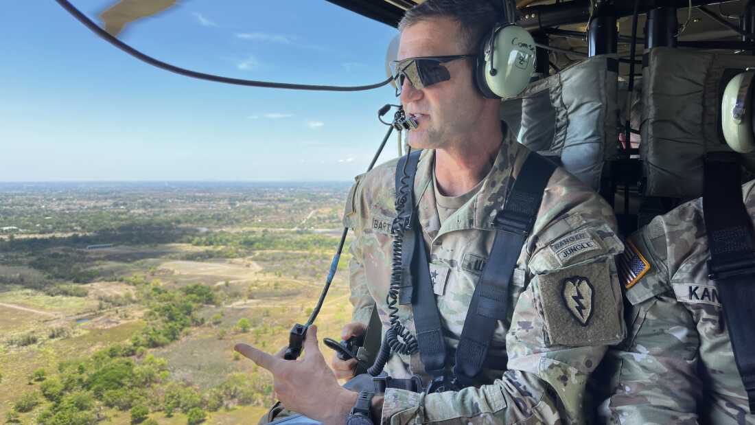 James B. Bartholomees III, wearing sunglasses and a camouflage-print uniform, sits in a Black Hawk helicopter looking out over the terrain of central Luzon island, which stretches out below.