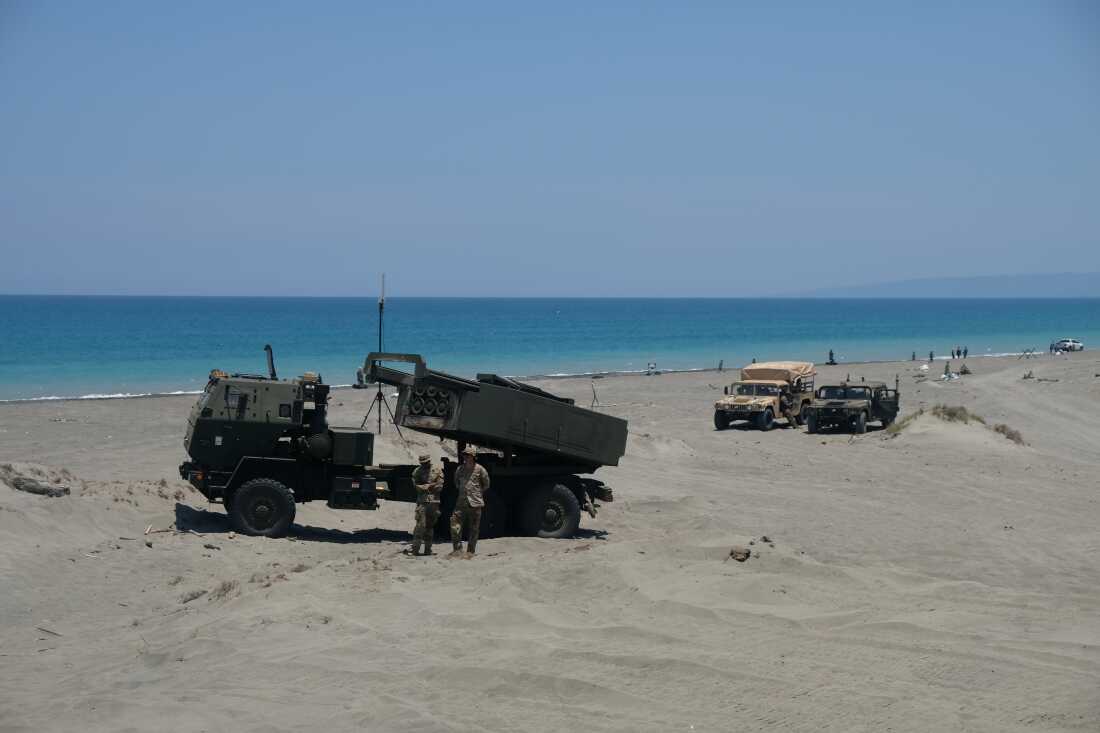 A high-mobility artillery rocket system (HIMARS) launcher sits on the beach of the La Paz sand dunes in Laoag City, Philippines. In the background are blue waters and a blue sky.