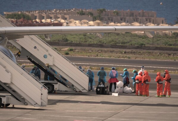 Passengers stand next to a Spanish government plane after disembarking from the hantavirus-stricken cruise ship MV Hondius at the airport in Tenerife, Canary Islands, Spain, Sunday, May 10, 2026. (AP Photo/Arturo Rodriguez)